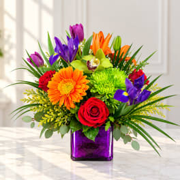 Colorful bouquet in a purple glass vase with roses, gerbera daisies, lilies, and irises