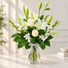 White roses and lilies arranged in a clear glass vase with a ribbon