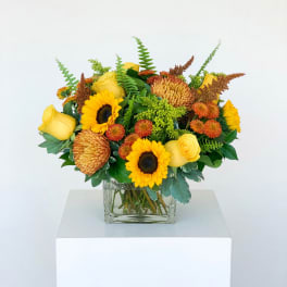 Yellow sunflower and rose arrangement in a clear square vase