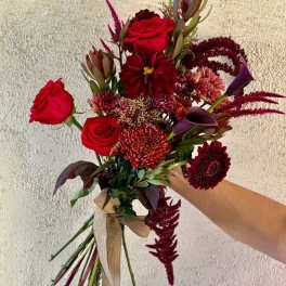 Hand-tied bouquet of red roses and burgundy mixed flowers with a ribbon wrap