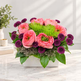 Pink and purple flowers arranged in a white rectangular container