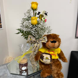 Yellow roses in a glass vase with a teddy bear and honey jar