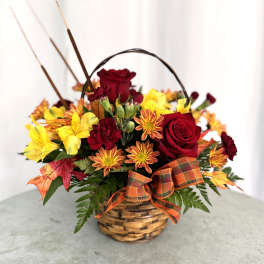 Basket arrangement of red roses and yellow flowers with an autumn ribbon