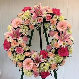 Heart-shaped floral wreath on a stand with pink lilies, roses, daisies, and carnations
