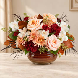Peach and red floral arrangement in a brown glass bowl vase