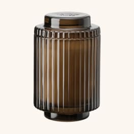 Amber ribbed glass jar with a black lid on a plain background
