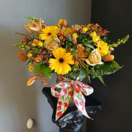 Yellow and orange mixed flower arrangement in a glass vase with a floral ribbon