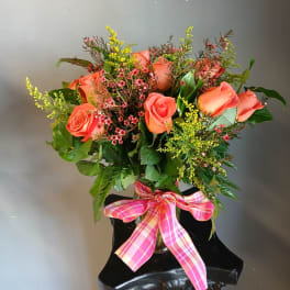 Orange roses in a glass vase with a pink plaid ribbon