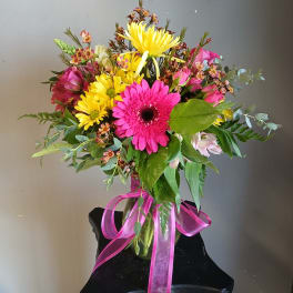 Mixed bouquet of pink and yellow flowers in a glass vase with a pink ribbon