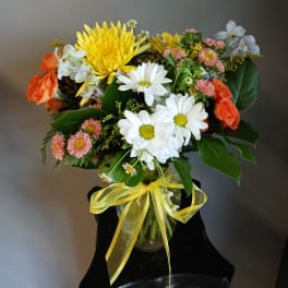 Mixed bouquet of daisies, roses, and chrysanthemums in a glass vase with a yellow ribbon.