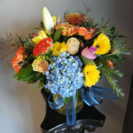 Mixed bouquet in a glass vase with blue hydrangea, roses, gerbera daisies, and lilies