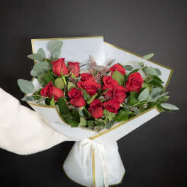 Bouquet of red roses wrapped in white paper with gold trim