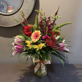 Colorful mixed flower arrangement in a glass vase with a patterned ribbon