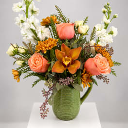 Peach roses and orange blooms in a green ceramic pitcher
