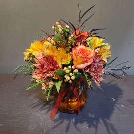 Mixed bouquet of orange, yellow, and pink flowers in an amber vase