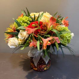 Mixed bouquet of roses, alstroemeria, and green hydrangeas in a ribboned vase