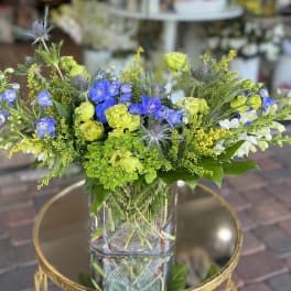 Mixed bouquet of blue, green, and white flowers in a clear glass vase