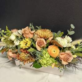 Low floral arrangement with peach roses, white blooms, and yellow chrysanthemums in a white box.