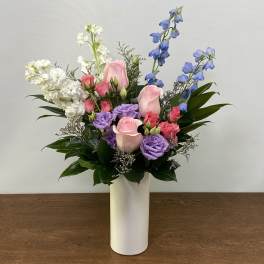 Mixed pink, purple, white, and blue flowers in a white vase
