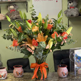 Orange lilies and roses in a glass vase with an orange ribbon