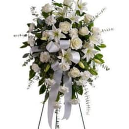 Tall standing spray of white roses, lilies, and carnations with a white ribbon on an easel