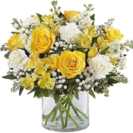Yellow roses and white flowers in a clear glass vase
