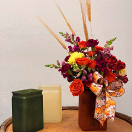 Orange and purple flower arrangement in a brown vase with a pumpkin ribbon