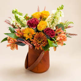 Mixed bouquet of yellow roses, carnations, chrysanthemums, and white blooms in a brown handled container