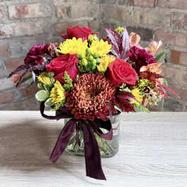 Bouquet of red roses and yellow chrysanthemums in a glass vase with a burgundy ribbon