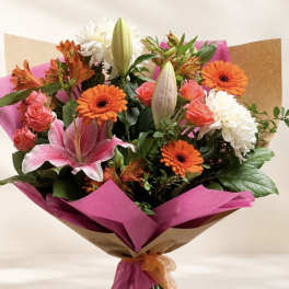 Bouquet of pink lilies, orange gerberas, roses, and white chrysanthemums wrapped in pink paper