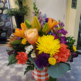 Mixed bouquet in a checkered container with lilies, roses, carnations, and chrysanthemums