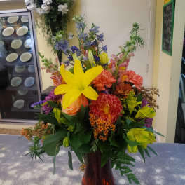 Colorful mixed bouquet in a tall vase with yellow lilies and orange blooms