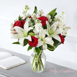 Arrangement of red roses and white lilies with white accent flowers in a clear glass vase