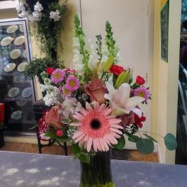 Mixed bouquet in a dark glass vase with pink gerbera, lilies, roses, and snapdragons