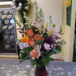 Mixed bouquet of lilies, roses, and daisies in a dark glass vase