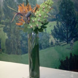 Tall vase arrangement with green orchids and orange tropical flowers