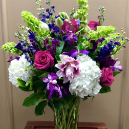 Tall mixed bouquet with pink roses, white hydrangeas, and purple orchids in a glass vase
