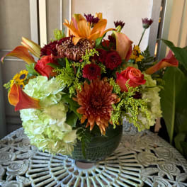 Mixed bouquet with orange lilies, roses, chrysanthemums, and pale hydrangeas in a green vase