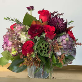 Bouquet of red roses, purple blooms, and hydrangeas in a metal container