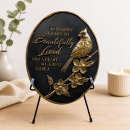 Oval memorial plaque with a gold bird and flowers on a stand