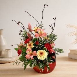 Mixed floral arrangement in a red vase with pink and yellow blooms