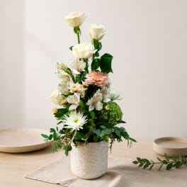 Tall floral arrangement with white roses and mixed blooms in a white textured vase