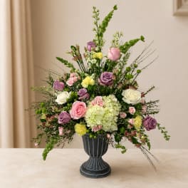 Mixed pink, purple, and white flowers in a dark pedestal vase