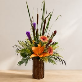 Tall tropical flower arrangement in a bark-covered vase with orange and purple blooms