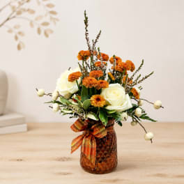 Orange and white flower arrangement in an amber vase with a plaid ribbon