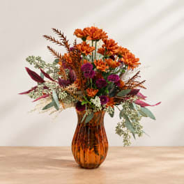 Orange and purple floral arrangement in an amber glass vase