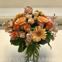 Mixed bouquet of orange and pink flowers in a clear glass vase