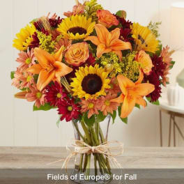 Bouquet of sunflowers, orange lilies, and mixed daisies in a glass vase