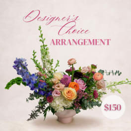Mixed floral arrangement in a pale pink vase with blue, pink, orange, and white blooms