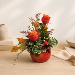 Two red roses in a red ceramic vase with autumn foliage
